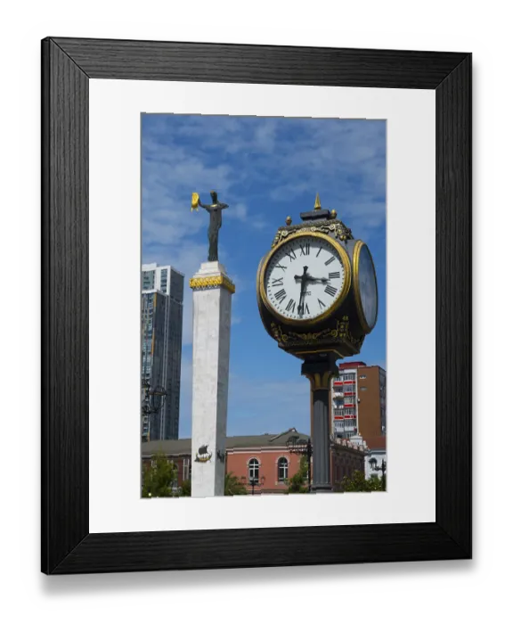 Framed Print : Large clock and statue in front of modern buildings under bright blue sky