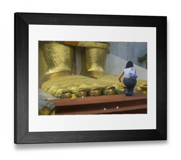 Framed Print : A young woman places flowers on the toes of the standing Buddha at Wat Indrawihan