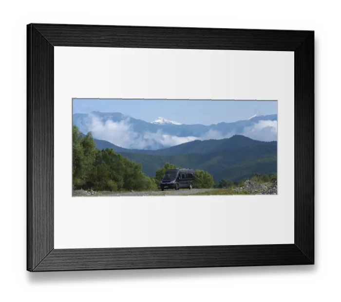 Framed Print : A black van on a road in a mountain valley with snowy peaks and clouds