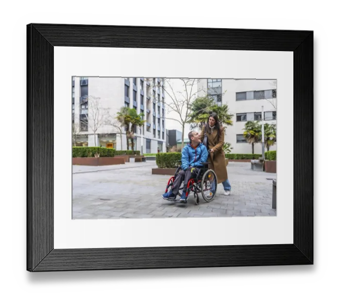 Framed Print : Woman pushing smiling man in a wheelchair along a city sidewalk