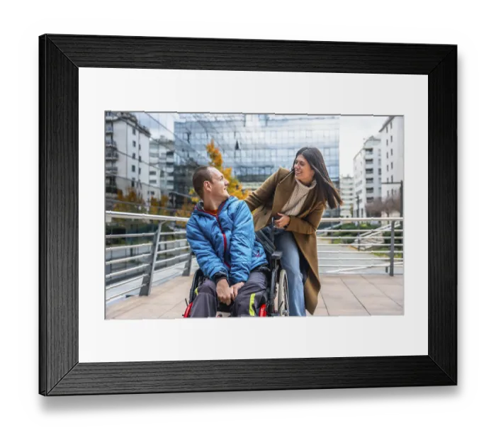 Framed Print : Young man in a wheelchair smiling and chatting with a supportive woman on a sunny urban street Framed Print : Young man in a wheelchair smiling and chatting with a supportive woman on a sunny urban street