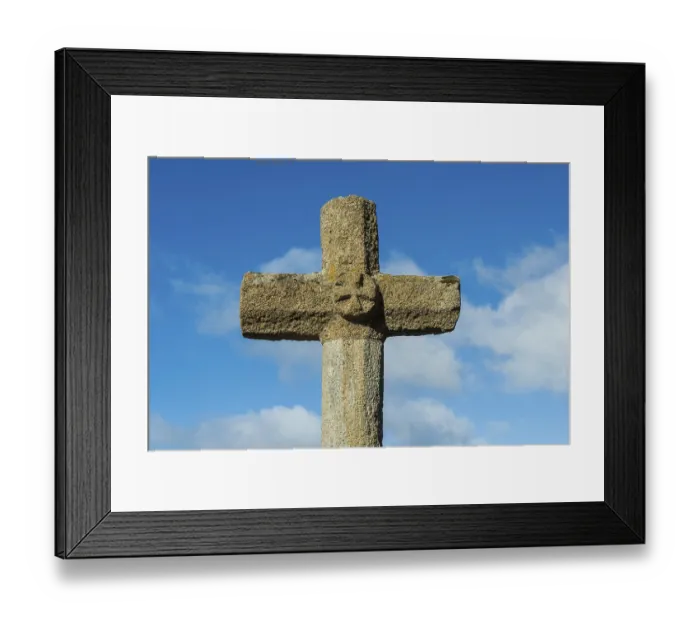 Framed Print : Stone cross stands tall against a bright blue sky with scattered white clouds in the background