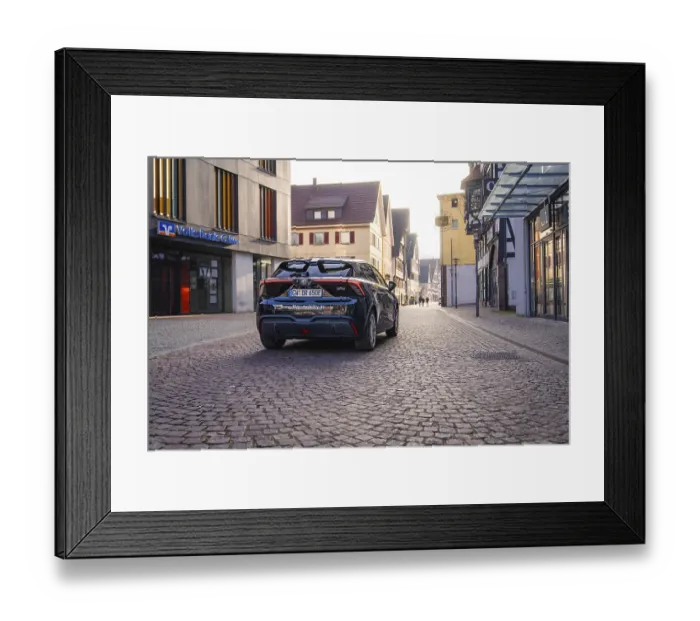 Framed Print : Black car on a paved street in the city with modern and historic architecture in the background at dusk