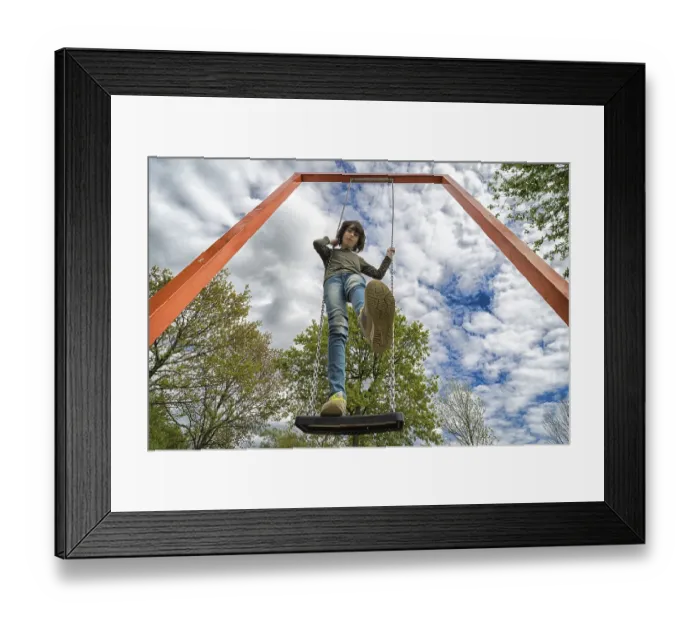 Framed Print : A boy stands on a swing. View from below