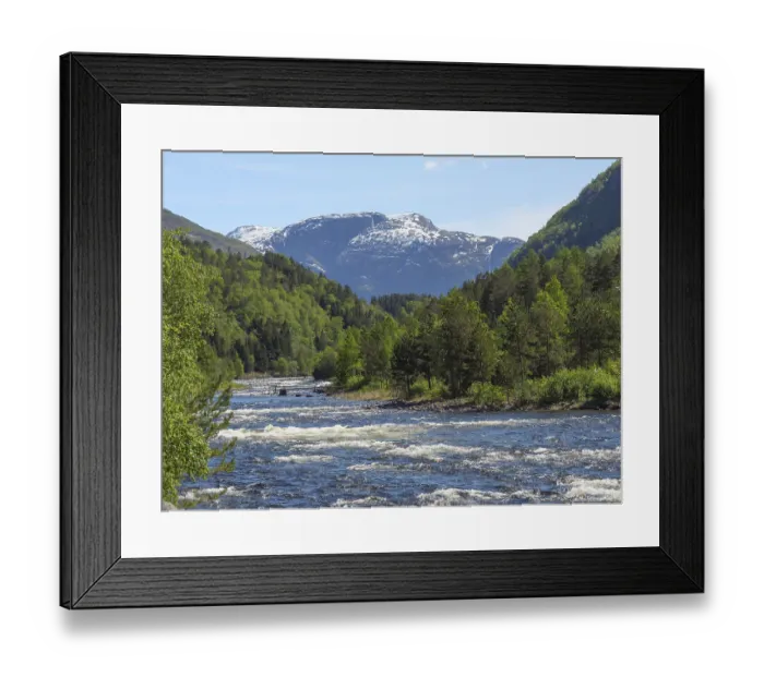 Framed Print : River in mountainous landscape with snow-capped peaks and green forests under blue sky Framed Print : River in mountainous landscape with snow-capped peaks and green forests under blue sky
