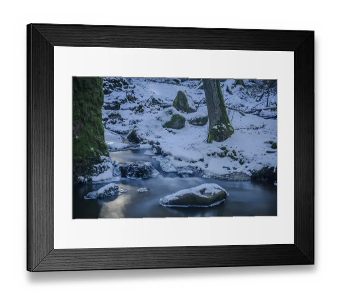 Framed Print : A small stream flows through a forest surrounded by snow