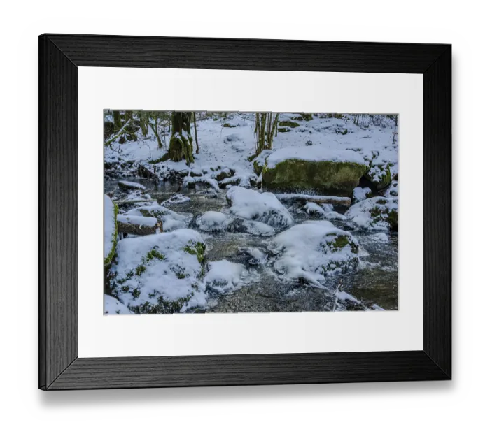 Framed Print : A stream flows in a forest that is covered with snow