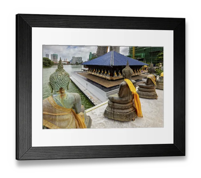 Framed Print : Buddha statues with yellow cloths sit in front of a modern cityscape on the water Framed Print : Buddha statues with yellow cloths sit in front of a modern cityscape on the water