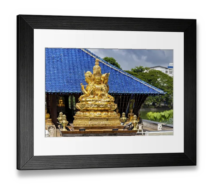 Framed Print : Golden Buddhist statue in front of a blue roof with cloudy sky