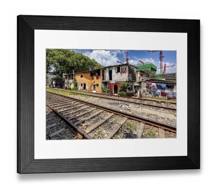 Framed Print : Construction cranes rise behind brightly painted houses along the train tracks under a blue sky