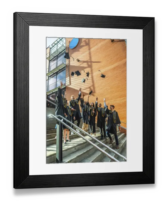 Framed Print : Diverse group of young adult university graduates celebrating a successful academic achievement by tossing their Framed Print : Diverse group of young adult university graduates celebrating a successful academic achievement by tossing their