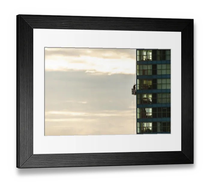 Framed Print : Person cleaning windows on a tall building against a cloudy sky in Toronto