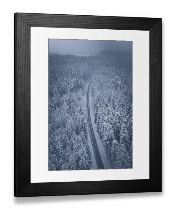 Framed Print : Snowy road snaking through a thick forest