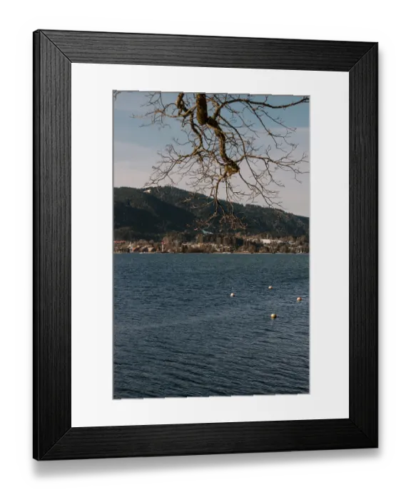 Framed Print : A calm lake with surrounding mountains and bare branches against a blue sky and buoys on the water