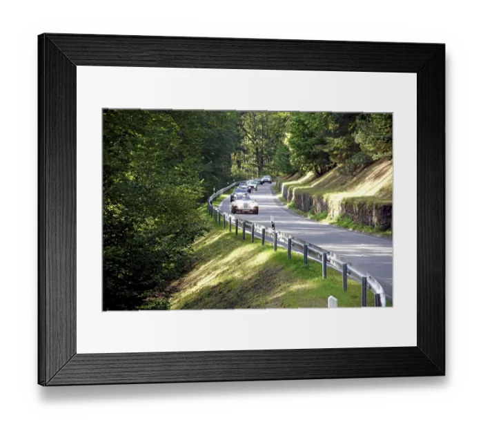 Framed Print : Several vintage cars drive on a winding country road through a sunny forest