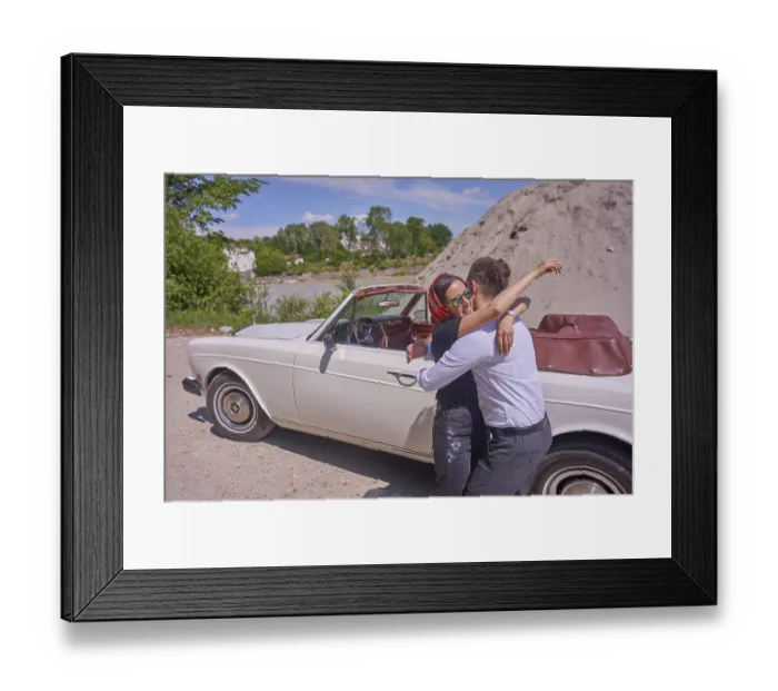 Framed Print : A couple embracing joyfully by a white convertible car on a sunny day next to building site of work