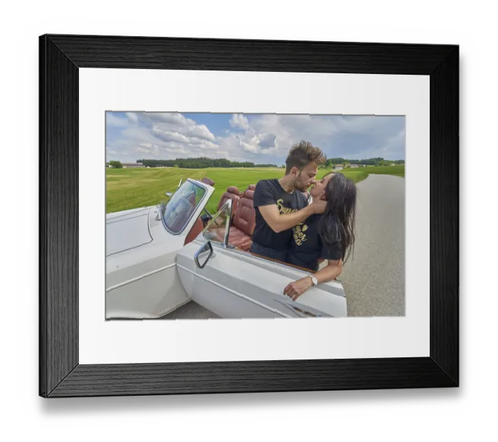 Framed Print : Couple kissing by a convertible car amidst a rustic countryside backdrop
