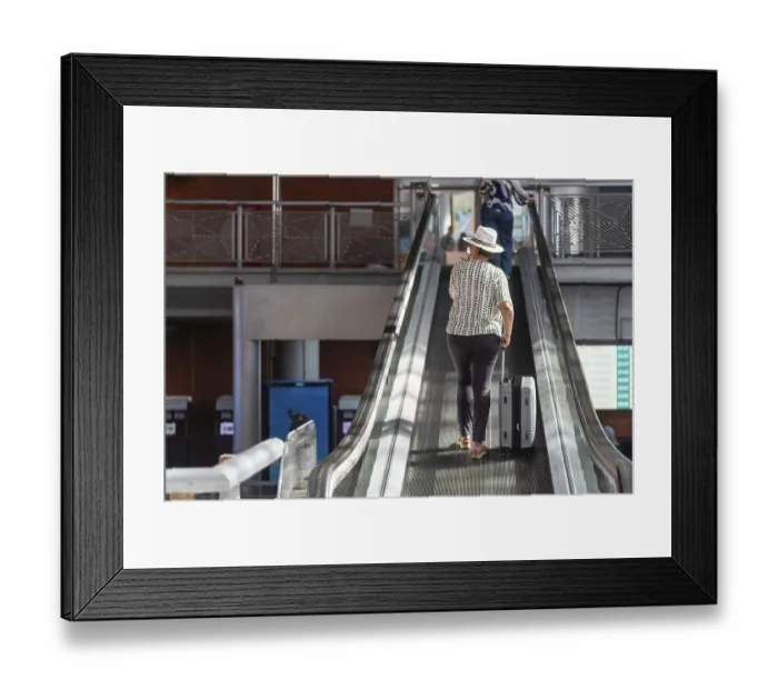Framed Print : Woman in a hat pulling luggage up an escalator