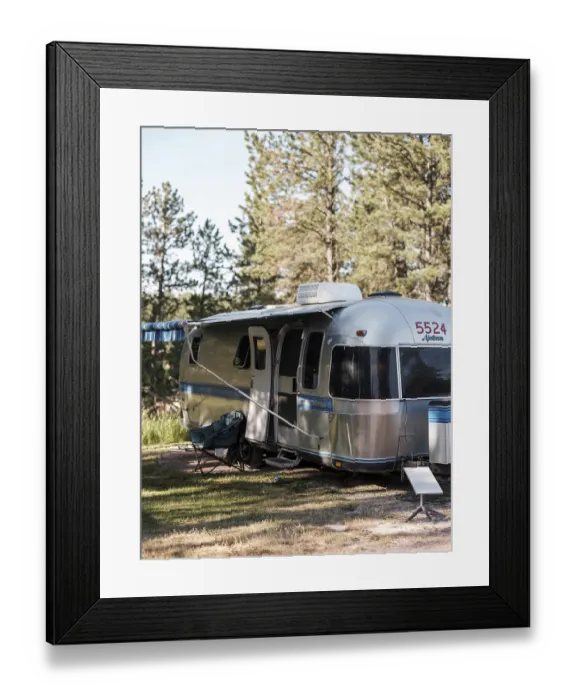 Framed Print : A silver Airstream camper is parked at a wooded campsite with trees surrounding it under daylight