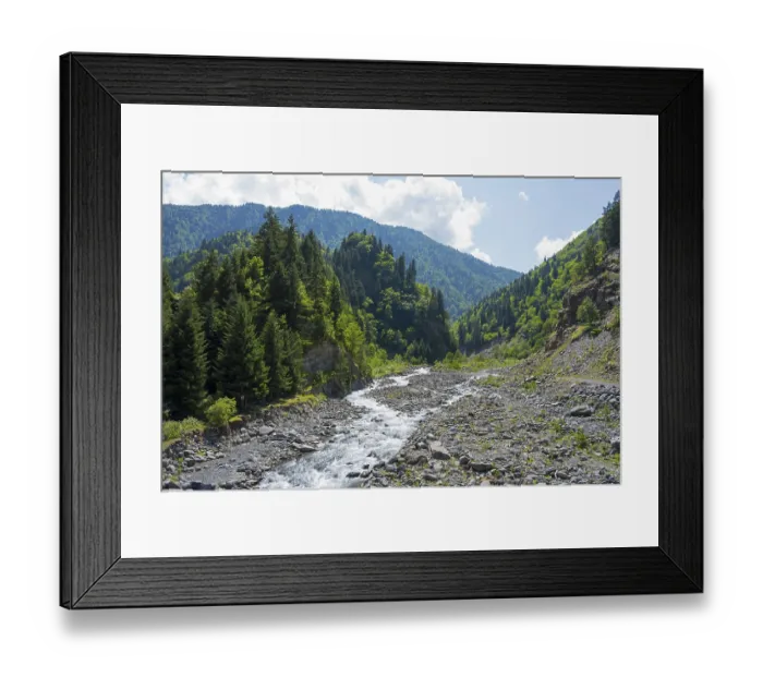 Framed Print : Wild stream flows through a stony forest path surrounded by green mountains under a blue sky Framed Print : Wild stream flows through a stony forest path surrounded by green mountains under a blue sky