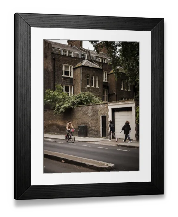Framed Print : Cyclist and pedestrians pass a historic brick building on a cloudy day in Greater London