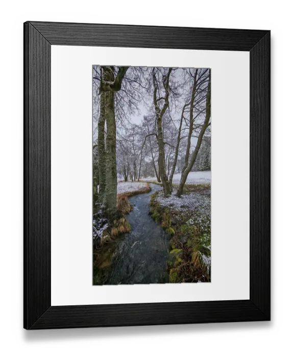 Framed Print : A stream snakes through a snow-covered forest landscape with bare trees