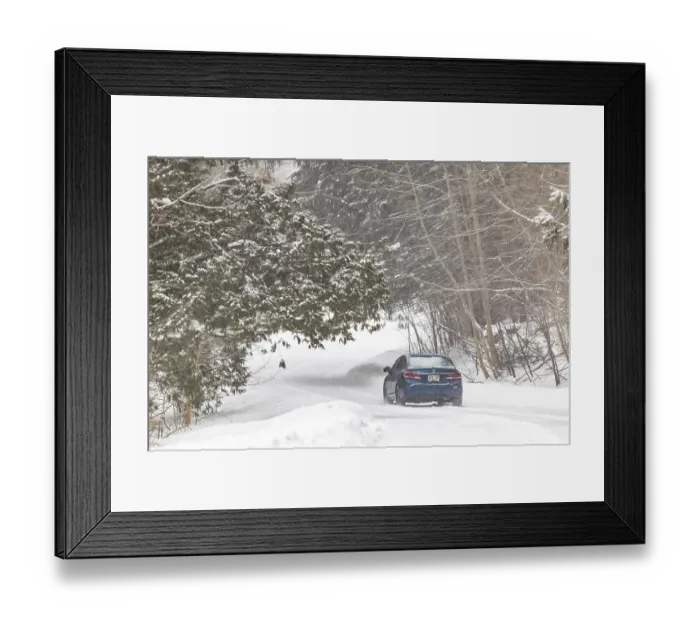 Framed Print : A blue car travels down a snow-covered road in a forest