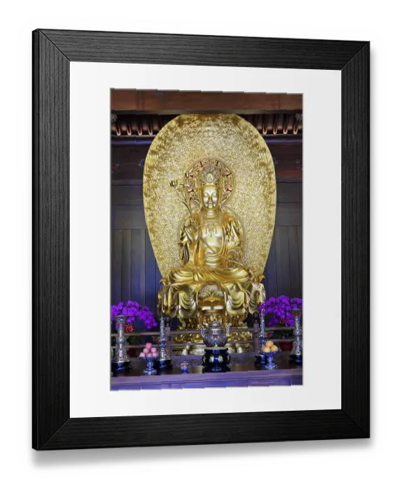 Framed Print : A large golden Buddha statue flanked by flowers in a temple