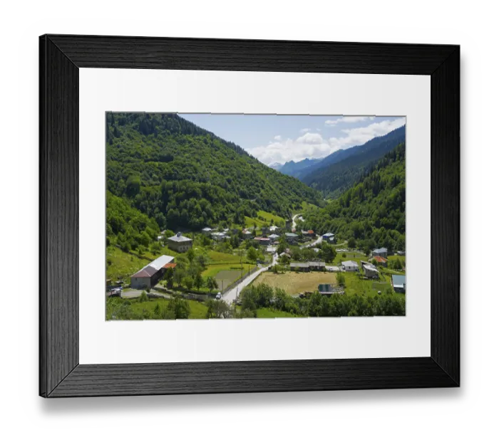 Framed Print : Village nestled in a green valley with mountains in the background