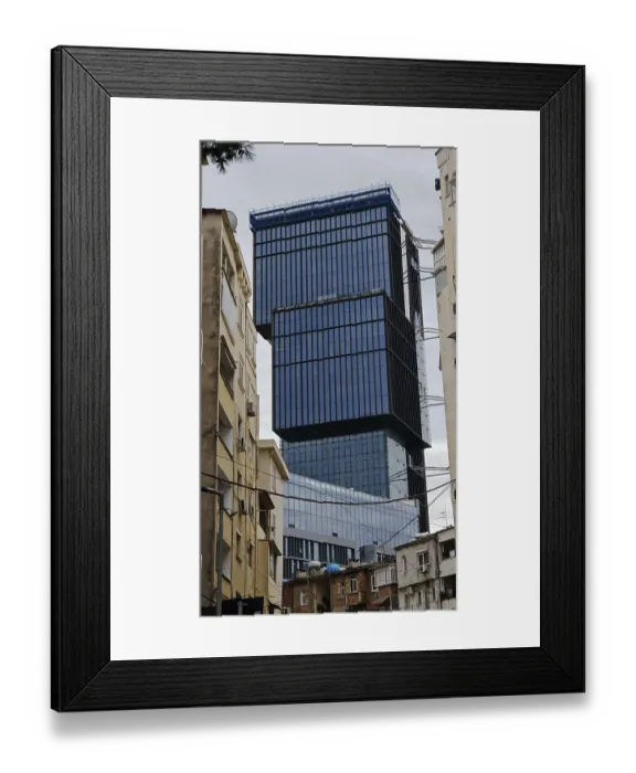 Framed Print : Modern high-rise building with glass facade between older buildings in an urban environment under cloudy sky