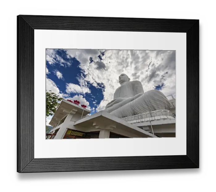 Framed Print : Large white Buddha statue under dramatic sky surrounded by temple architecture and clouds Framed Print : Large white Buddha statue under dramatic sky surrounded by temple architecture and clouds