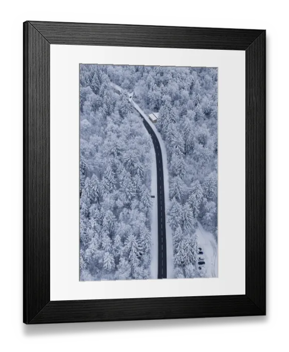 Framed Print : Snowy road snaking through a thick winter forest