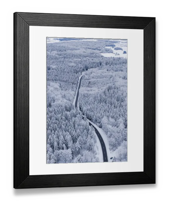 Framed Print : Snowy road snakes through a thick winter forest