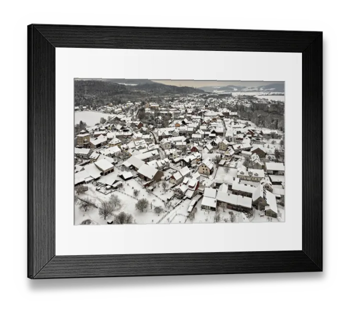 Framed Print : Village in winter with snow-covered half-timbered houses and trees under grey skies