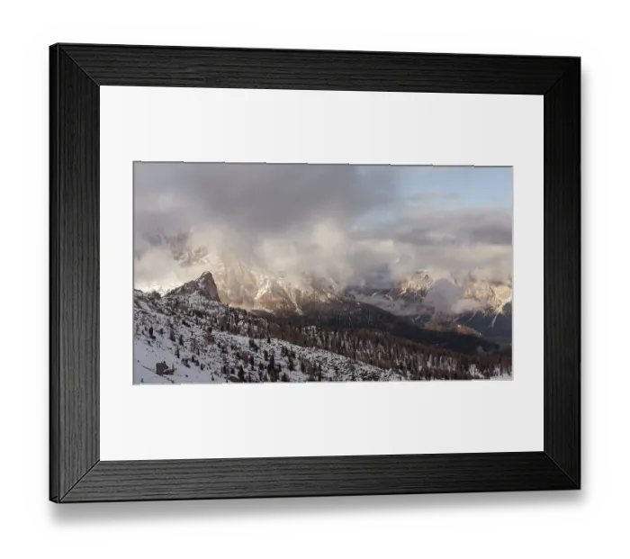 Framed Print : Snowy mountains under a cloudy sky with scattered sunlight