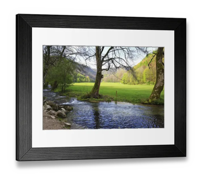 Framed Print : A calm river flows through a green meadow with wooded hills in the background