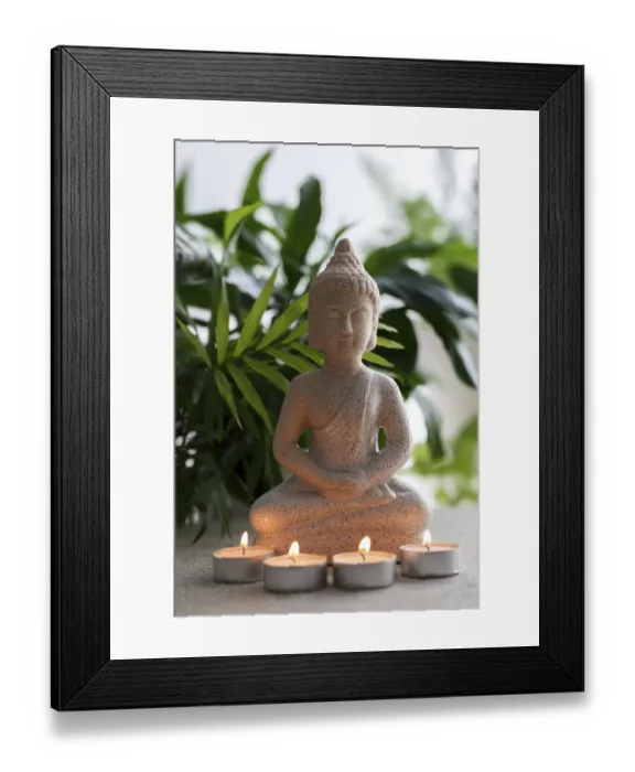 Framed Print : Natural stone statue of Buddha sitting in meditation surrounded by candles and tropical plants Framed Print : Natural stone statue of Buddha sitting in meditation surrounded by candles and tropical plants