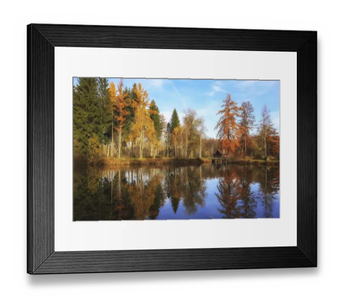 Framed Print : A lake reflecting autumn trees and a small hut under a blue sky