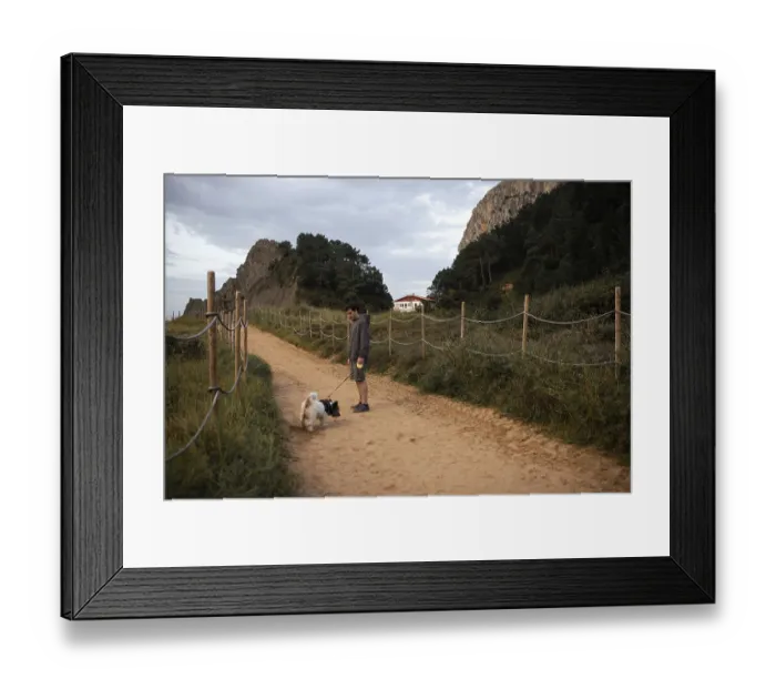 Framed Print : A person walks their dog along a sandy path surrounded by lush greenery and rocky cliffs in Ea