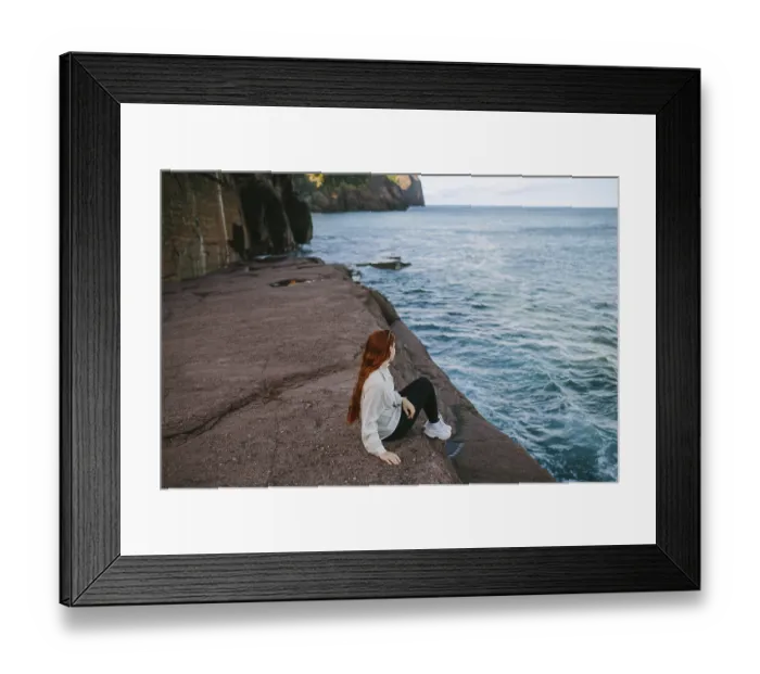 Framed Print : A woman enjoys a serene moment sitting on a rocky ledge overlooking the waves at Flatrock