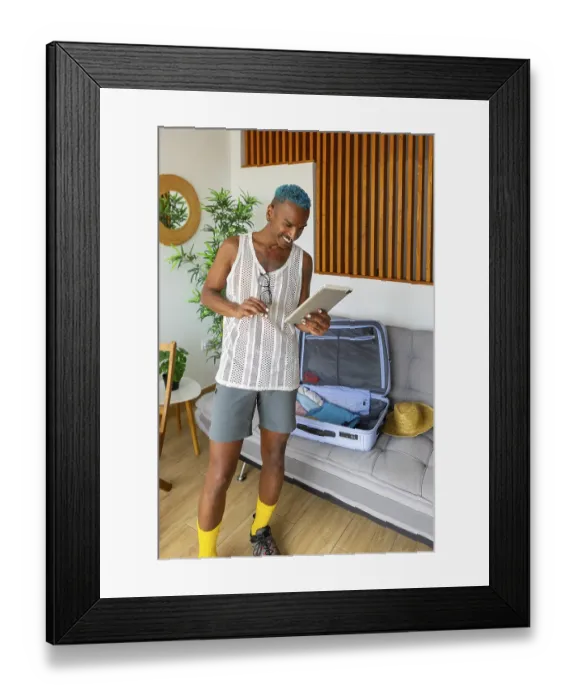 Framed Print : A joyful LGBTQIA+ man with vibrant blue hair packs a suitcase while smiling at a tablet Framed Print : A joyful LGBTQIA+ man with vibrant blue hair packs a suitcase while smiling at a tablet