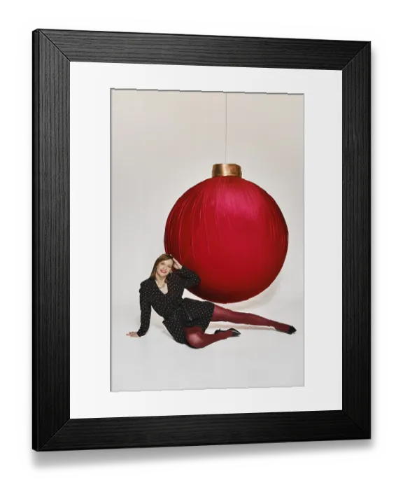 Framed Print : A woman is sitting on the floor next to a large red ornament in a studio setting