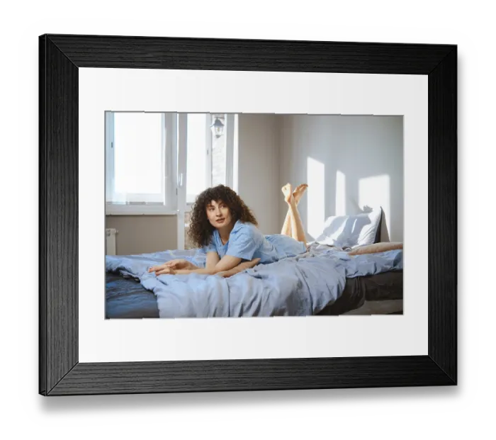 Framed Print : A woman with curly hair lays on a bed with light blue sheets Framed Print : A woman with curly hair lays on a bed with light blue sheets