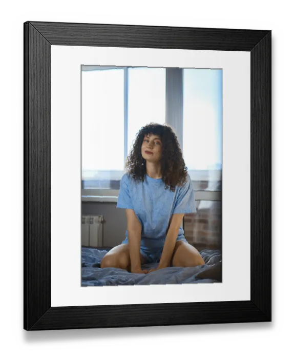 Framed Print : A woman sits on a bed in front of a large window