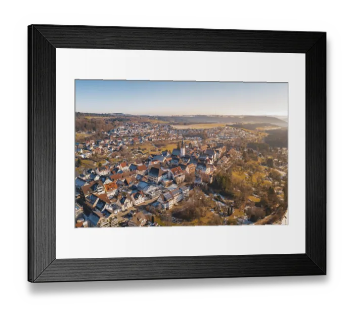 Framed Print : Aerial view of a town with a central church surrounded by red roofs and winter landscape under blue sky