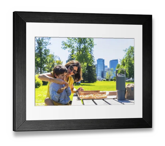Framed Print : Mother helps her son eat a slice of pizza at a picnic table in a calgary park