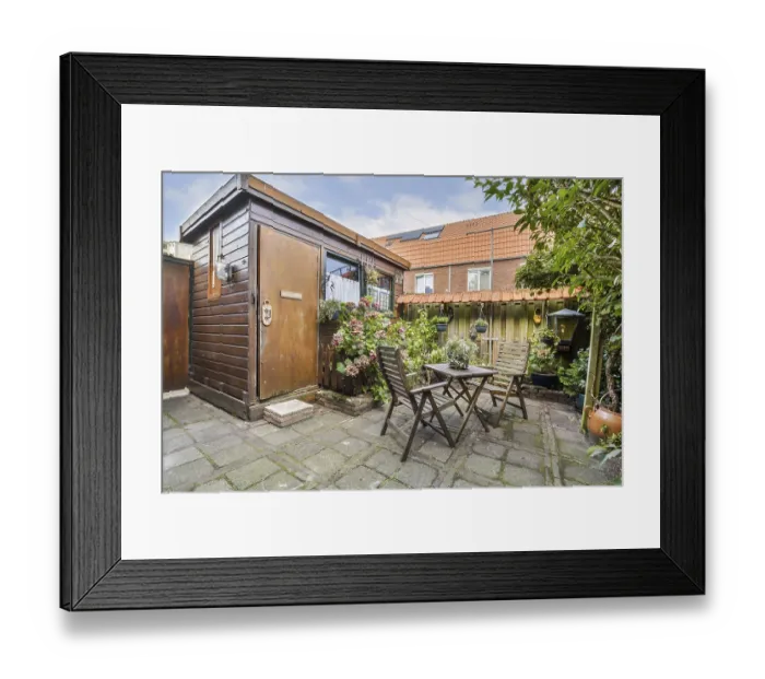 Framed Print : A serene backyard showcasing a wooden shed surrounded by vibrant flowers and a quaint seating area