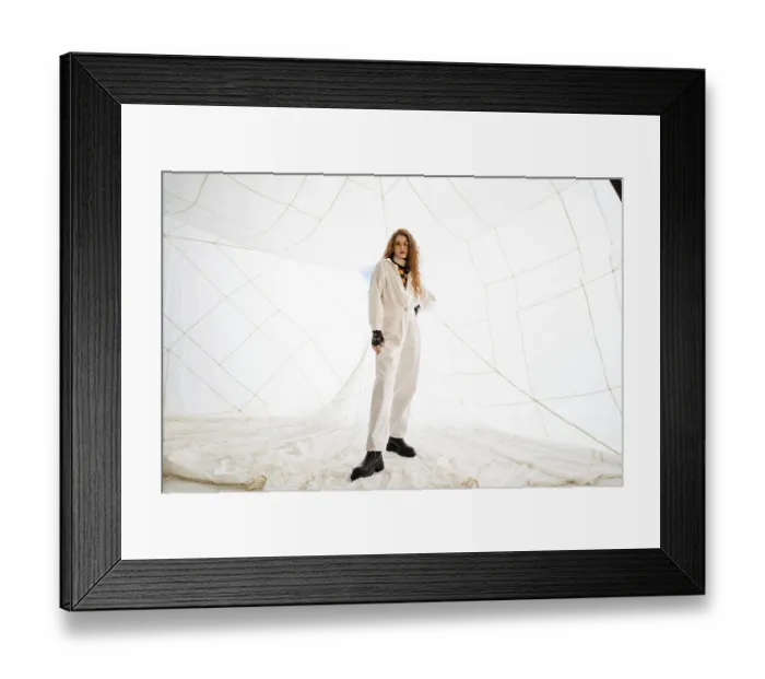 Framed Print : A woman in a white jumpsuit poses in front of a white netting background