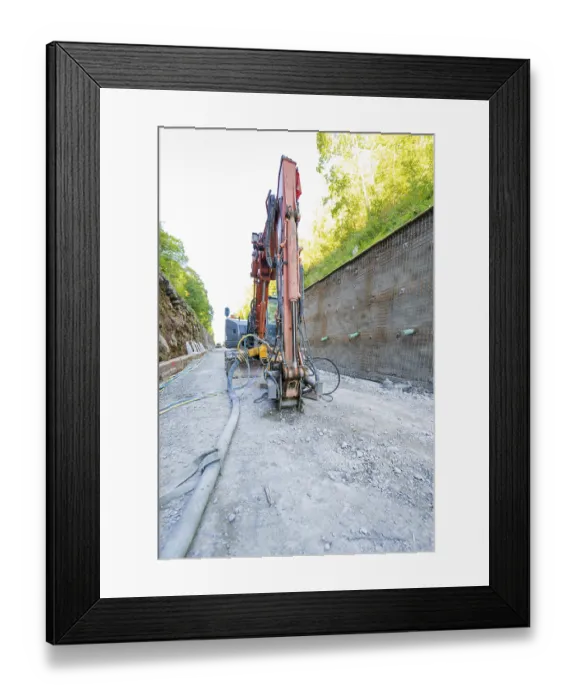 Framed Print : Excavator in action on a construction site next to a concrete wall with pipes