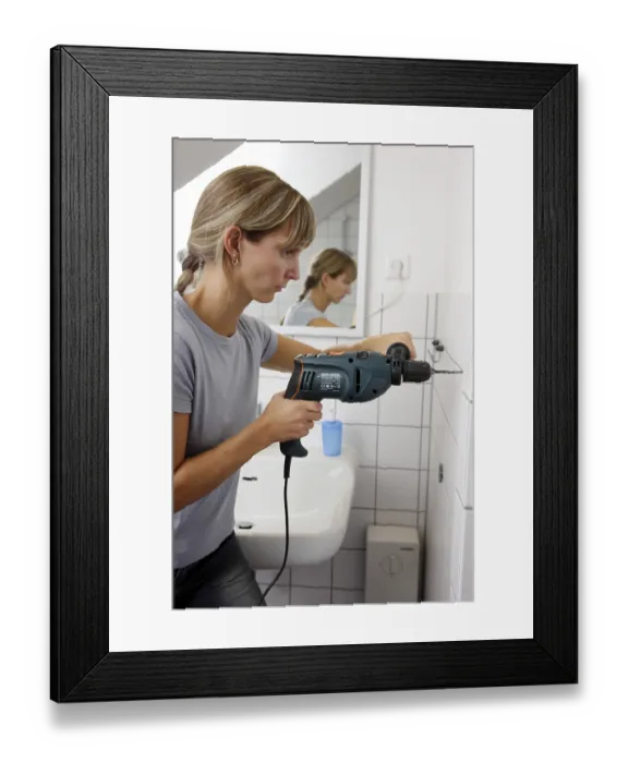 Framed Print : Young woman drilling a hole into a tiled bathroom wall